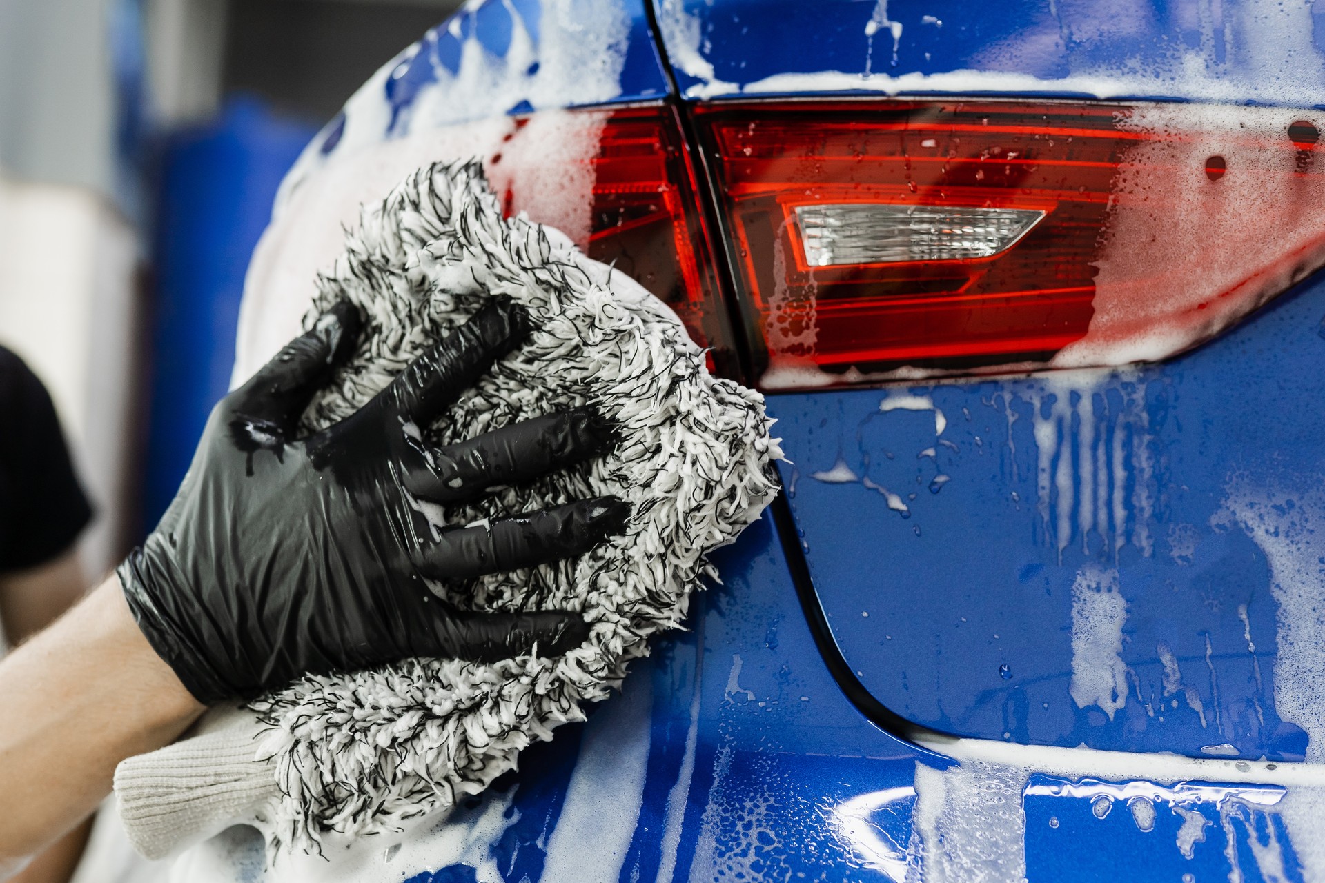 Hand washing with microfiber glove with foam car body in garage. Car washer doing manual foam washing in auto detailing service.